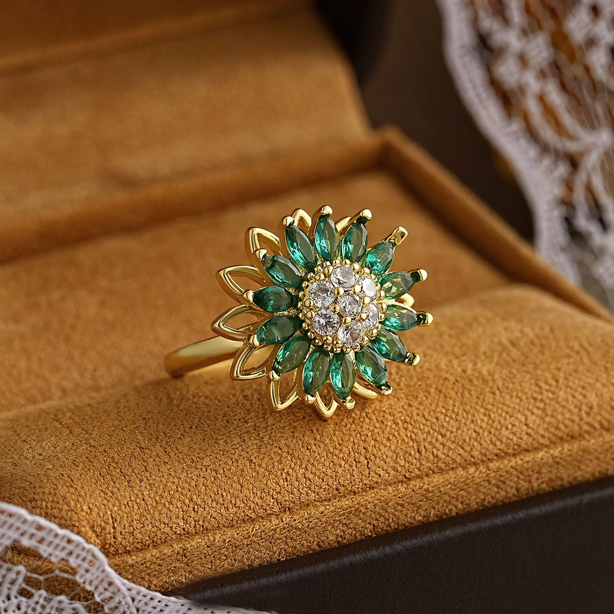 Close up of Solis anti-tarnish sunflower ring with emerald green and clear stones on textured leather