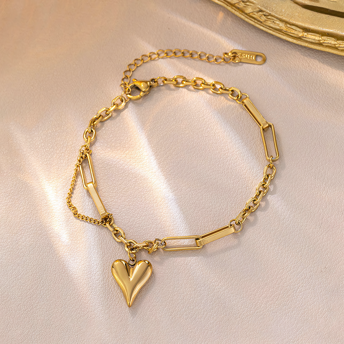 Amora anti-tarnish gold heart charm bracelet displayed on shimmering champagne silk