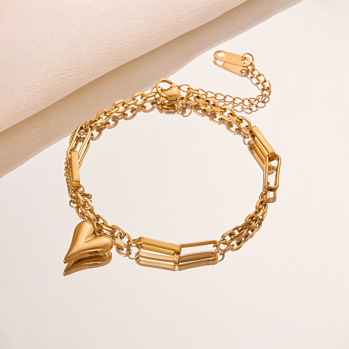 Amora gold plated heart charm bracelet reflected on a round mirror surface with paperclip links