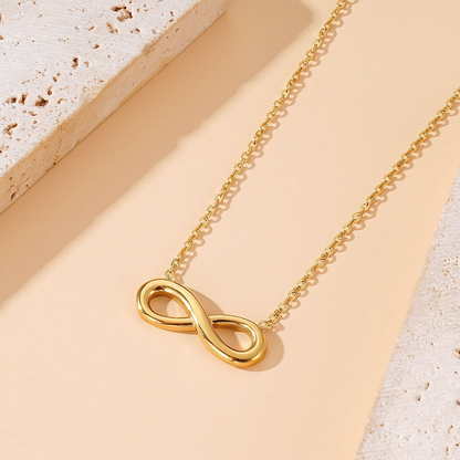 Aura gold anti-tarnish infinity necklace angled on a light beige surface next to stone