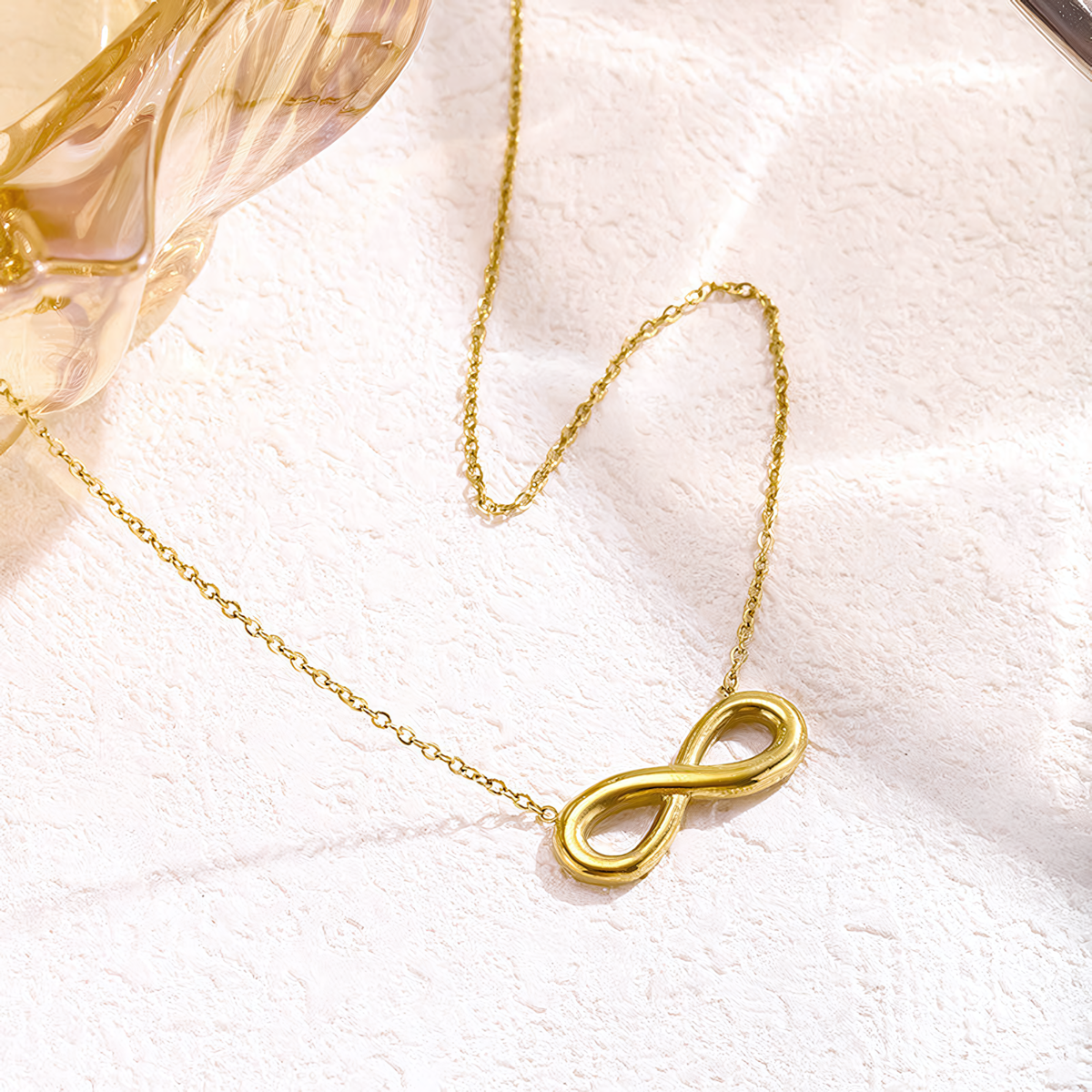 Close up of the Aura gold anti-tarnish infinity pendant resting on soft pink fabric