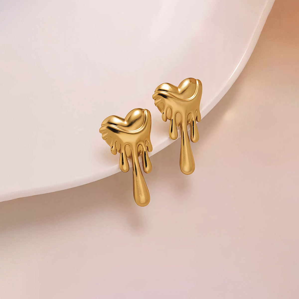 Close up of the Celeste 18K gold liquid metal heart earrings resting on a white ceramic plate