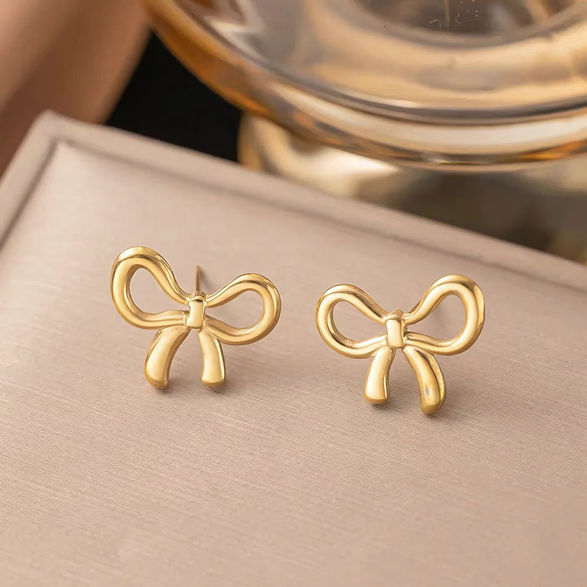 Clara 18K gold plated bow earrings displayed on a beige jewelry box