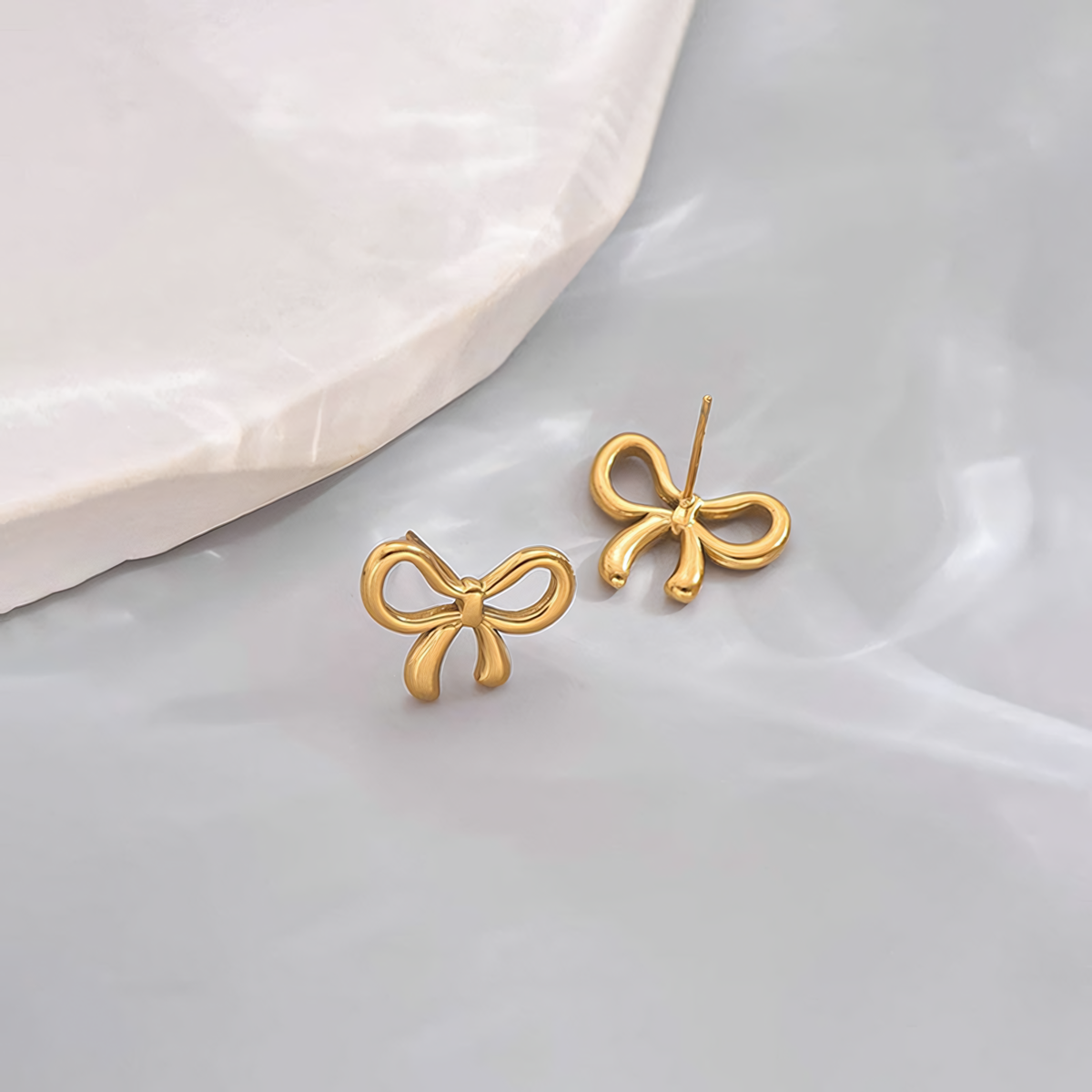 Angled view of the Clara 18K gold bow earrings showing the secure hypoallergenic stainless steel post