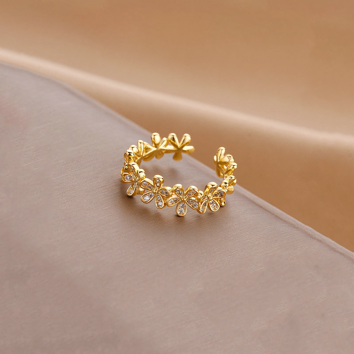 Fleur anti-tarnish gold floral open band ring resting on a folded taupe display surface