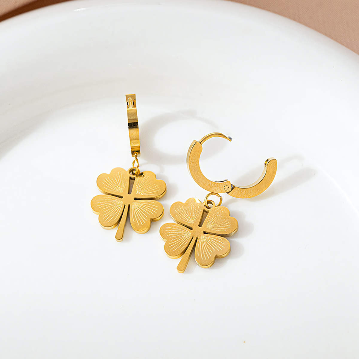 Ivy gold clover charm earrings with huggie hoops resting on a white ceramic plate