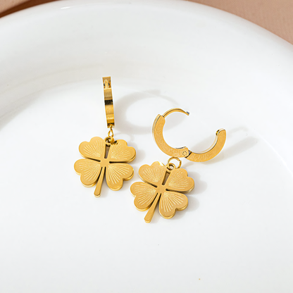 Ivy gold clover charm earrings with huggie hoops resting on a white ceramic plate