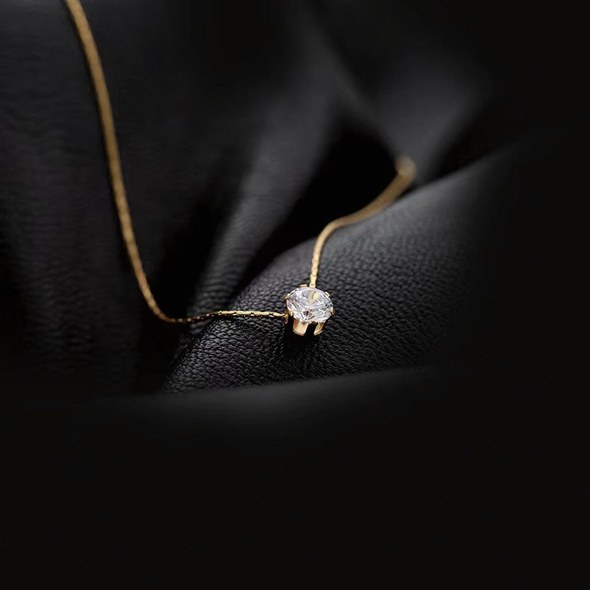 Macro shot of the Lumi anti-tarnish gold solitaire necklace catching light on dark textured leather