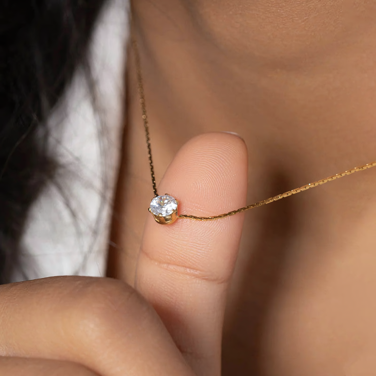 Close up of the Lumi anti-tarnish gold chain and brilliant solitaire crystal pendant resting on a finger