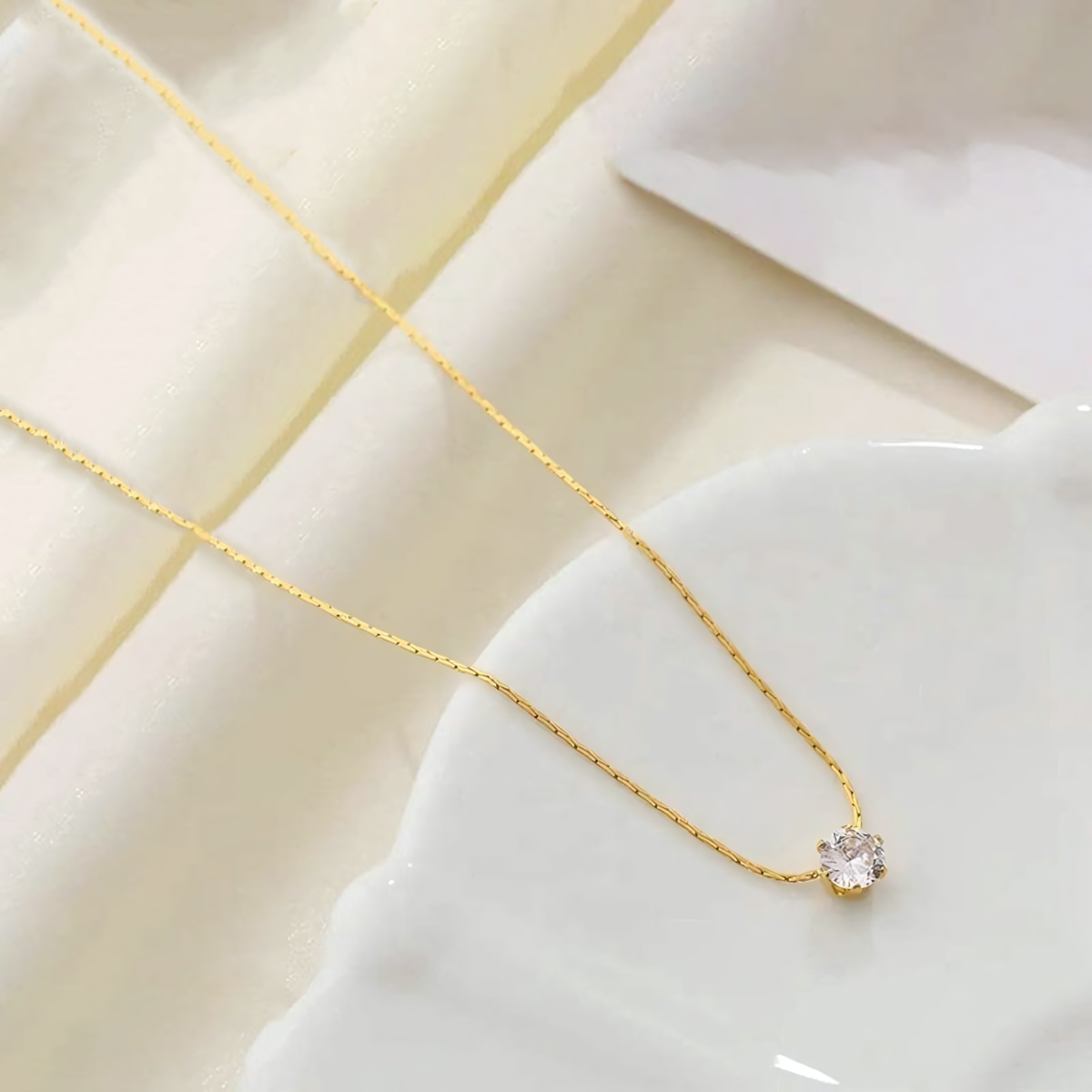 Lumi anti-tarnish gold necklace with clear solitaire crystal flat lay on white ceramic ruffle
