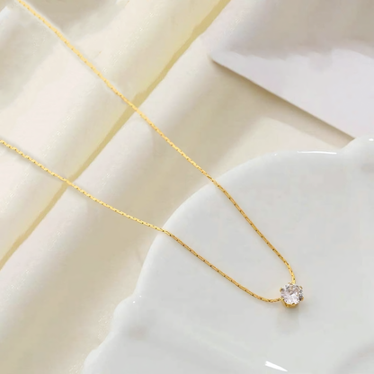 Lumi anti-tarnish gold necklace with clear solitaire crystal flat lay on white ceramic ruffle