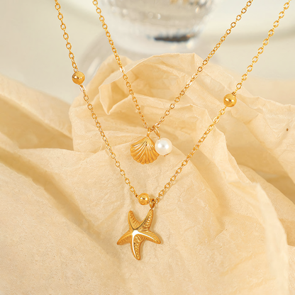 Marina anti-tarnish gold layered necklace with starfish and seashell pearl pendants resting on textured paper