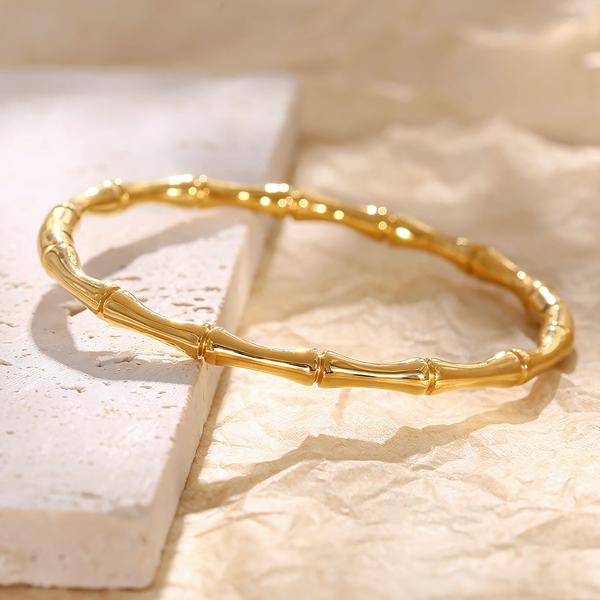 Mila anti-tarnish gold bamboo bracelet flat lay on a textured white stone surface