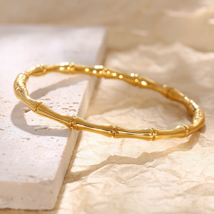Mila anti-tarnish gold bamboo bracelet flat lay on a textured white stone surface