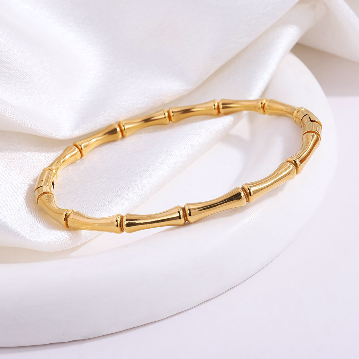 Top view of the Mila anti-tarnish gold bamboo bracelet resting on a white circular display platform