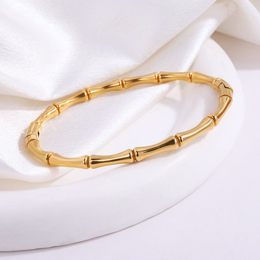 Top view of the Mila anti-tarnish gold bamboo bracelet resting on a white circular display platform
